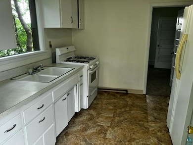 Kitchen featuring white appliances, light countertops, white cabinets, and stone finish floors