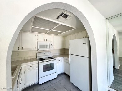 Kitchen with white appliances, white cabinets, tile counters, cooling unit, and dark tile patterned flooring
