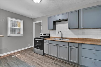 Kitchen featuring gray cabinetry, stainless steel range with electric cooktop, light wood-type flooring, tasteful backsplash, and a textured ceiling
