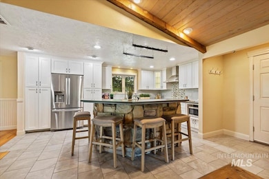 Kitchen with appliances with stainless steel finishes, wall chimney exhaust hood, white cabinetry, a kitchen breakfast bar, and tasteful backsplash