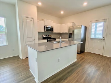 Kitchen with white cabinets, stainless steel appliances, a kitchen island with sink, dark wood finished floors, and recessed lighting