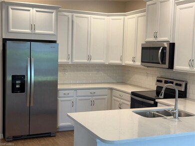 Kitchen featuring stainless steel appliances, white cabinetry, decorative backsplash, and wood finished floors