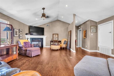 Living room featuring ceiling fan, wood finished floors, a fireplace, vaulted ceiling, and baseboards