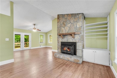 Unfurnished living room featuring light wood-style floors, a fireplace, a ceiling fan, baseboards, and lofted ceiling