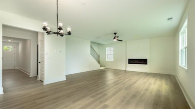 Unfurnished living room featuring a chandelier, a ceiling fan, light wood-style floors, and baseboards