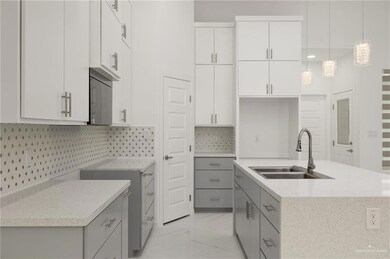 Kitchen with a sink, light marble finish flooring, gray cabinetry, and a center island with sink
