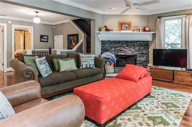 Living area featuring wood finished floors, a ceiling fan, crown molding, a stone fireplace, and baseboards