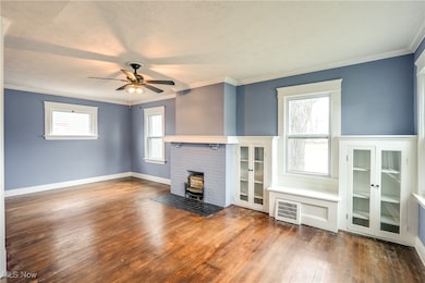 Unfurnished living room featuring crown molding, dark hardwood floors, built-in cabinets, and ceiling fan. Most windows updated.