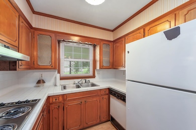 Kitchen with white appliances, a sink, crown molding, decorative backsplash, and under cabinet range hood