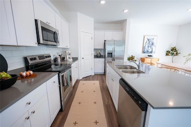 Kitchen with appliances with stainless steel finishes, a sink, dark wood-type flooring, decorative backsplash, and white cabinets