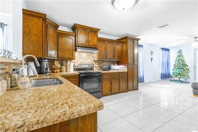 Kitchen with electric range, under cabinet range hood, decorative backsplash, light stone countertops, and light tile patterned flooring