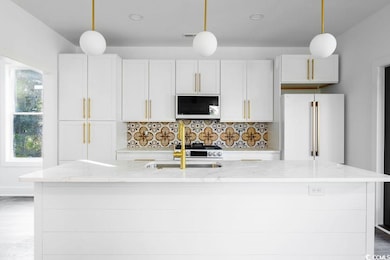 Kitchen featuring white microwave, tasteful backsplash, a center island with sink, light stone counters, and freestanding refrigerator
