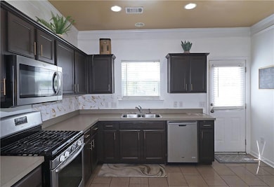 Kitchen with stainless steel appliances, a sink, light tile patterned floors, crown molding, and recessed lighting