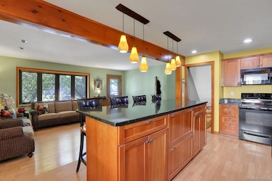 Kitchen with a breakfast bar, black appliances, pendant lighting, light wood-style flooring, and recessed lighting