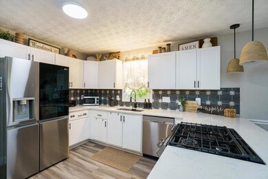 The Renovated Kitchen shines with White Shaker Cabinetry, Quartz Countertops, Custom Backsplash, and Premium Stainless-Steel Appliances, offering seamless flow to both Dining and Living Areas.