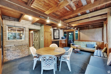 Carpeted enclosed deck with brick wall and a wood ceiling with exposed beams