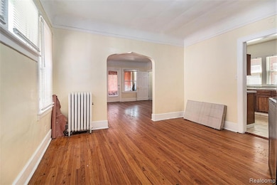 Unfurnished room featuring arched walkways, hardwood / wood-style floors, radiator heating unit, and crown molding