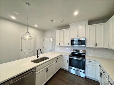 Kitchen featuring white cabinetry, sink, pendant lighting, dark wood-type flooring, and stainless steel appliances