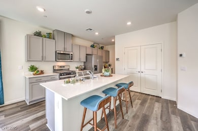 Kitchen with a kitchen bar, appliances with stainless steel finishes, light wood finished floors, a kitchen island with sink, and recessed lighting. Photo is representational only; actual home finishes may vary.