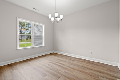 Spare room featuring a chandelier, baseboards, light wood-style floors, and healthy amount of natural light