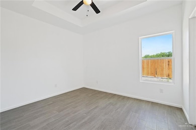 Unfurnished room featuring ceiling fan, a tray ceiling, baseboards, and wood finished floors