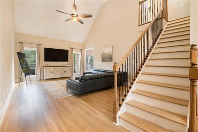Living room with stairway, high vaulted ceiling, ceiling fan, wood finished floors, and baseboards