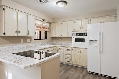 Kitchen featuring white appliances, light countertops, a peninsula, dark wood finished floors, and light brown cabinetry
