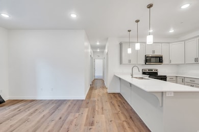 Kitchen featuring light wood-style flooring, appliances with stainless steel finishes, hanging light fixtures, a kitchen breakfast bar, and a peninsula