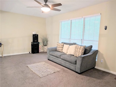 Carpeted living area featuring a ceiling fan and baseboards