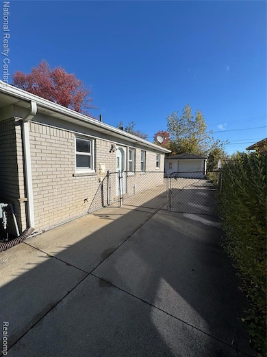 View of front of home featuring a gate, brick siding, a patio area, and an outbuilding