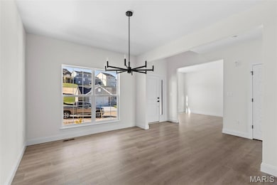Unfurnished dining area with hardwood / wood-style floors and an inviting chandelier