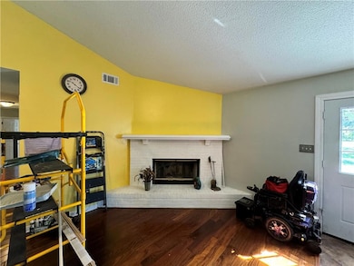 Living room featuring wood finished floors, a textured ceiling, vaulted ceiling, and a fireplace
