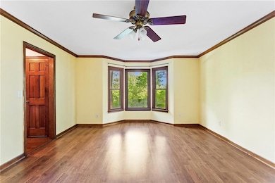 Empty room featuring wood finished floors, a ceiling fan, and crown molding