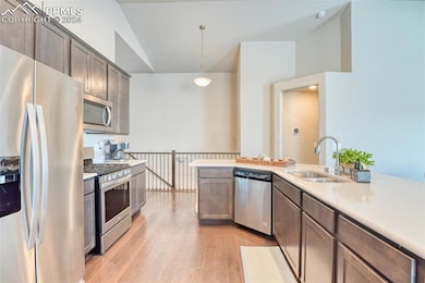 Kitchen with sink, stainless steel appliances, lofted ceiling, decorative light fixtures, and light wood-type flooring