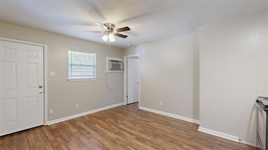 Unfurnished living room featuring a textured ceiling, wood finished floors, ceiling fan, and a wall mounted air conditioner
