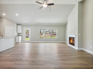 Unfurnished living room with a glass covered fireplace, a ceiling fan, recessed lighting, vaulted ceiling, and light wood-style floors