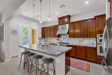 Kitchen with brown cabinetry, a breakfast bar, backsplash, appliances with stainless steel finishes, and light stone counters