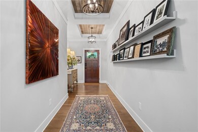 Entryway with a chandelier, wood finished floors, baseboards, crown molding, and a raised ceiling