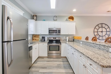 Kitchen featuring light wood finished floors, a peninsula, white cabinets, appliances with stainless steel finishes, and crown molding