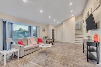 Living room with stairway, light wood-style floors, recessed lighting, and high vaulted ceiling