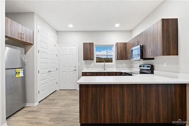 Kitchen with sink, appliances with stainless steel finishes, dark brown cabinets, light hardwood / wood-style floors, and kitchen peninsula