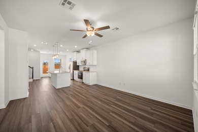 Kitchen featuring pendant lighting, ceiling fan, appliances with stainless steel finishes, white cabinetry, and a kitchen island