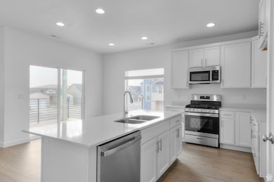 Kitchen featuring stainless steel appliances, white cabinetry, an island with sink, recessed lighting, and light wood-style floors