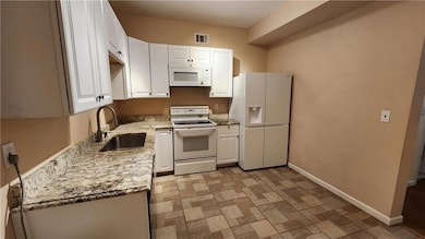 Kitchen with white appliances, a sink, white cabinets, light stone counters, and baseboards