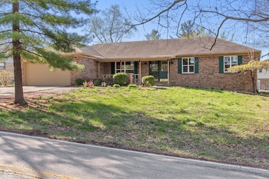 ranch-style house with a porch, a front lawn, brick siding, a garage, and driveway