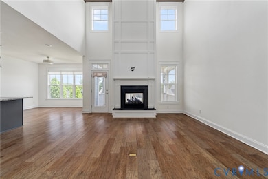 Unfurnished living room featuring a high ceiling, plenty of natural light, a multi sided fireplace, and dark wood-style floors