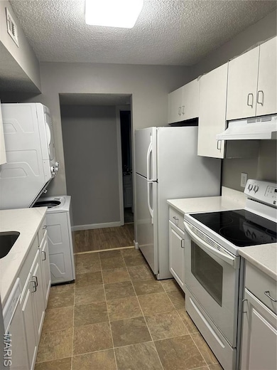 Kitchen with light countertops, stove, stacked washer / drying machine, range hood, and a textured ceiling