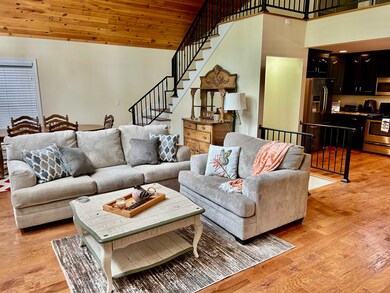Living room with lofted ceiling, stairs, light woo