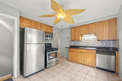 Kitchen with dark countertops, appliances with stainless steel finishes, tasteful backsplash, light tile patterned flooring, and brown cabinetry