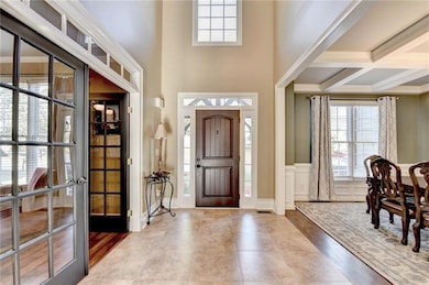 Foyer with healthy amount of natural light, beam ceiling, coffered ceiling, wainscoting, and tile patterned flooring